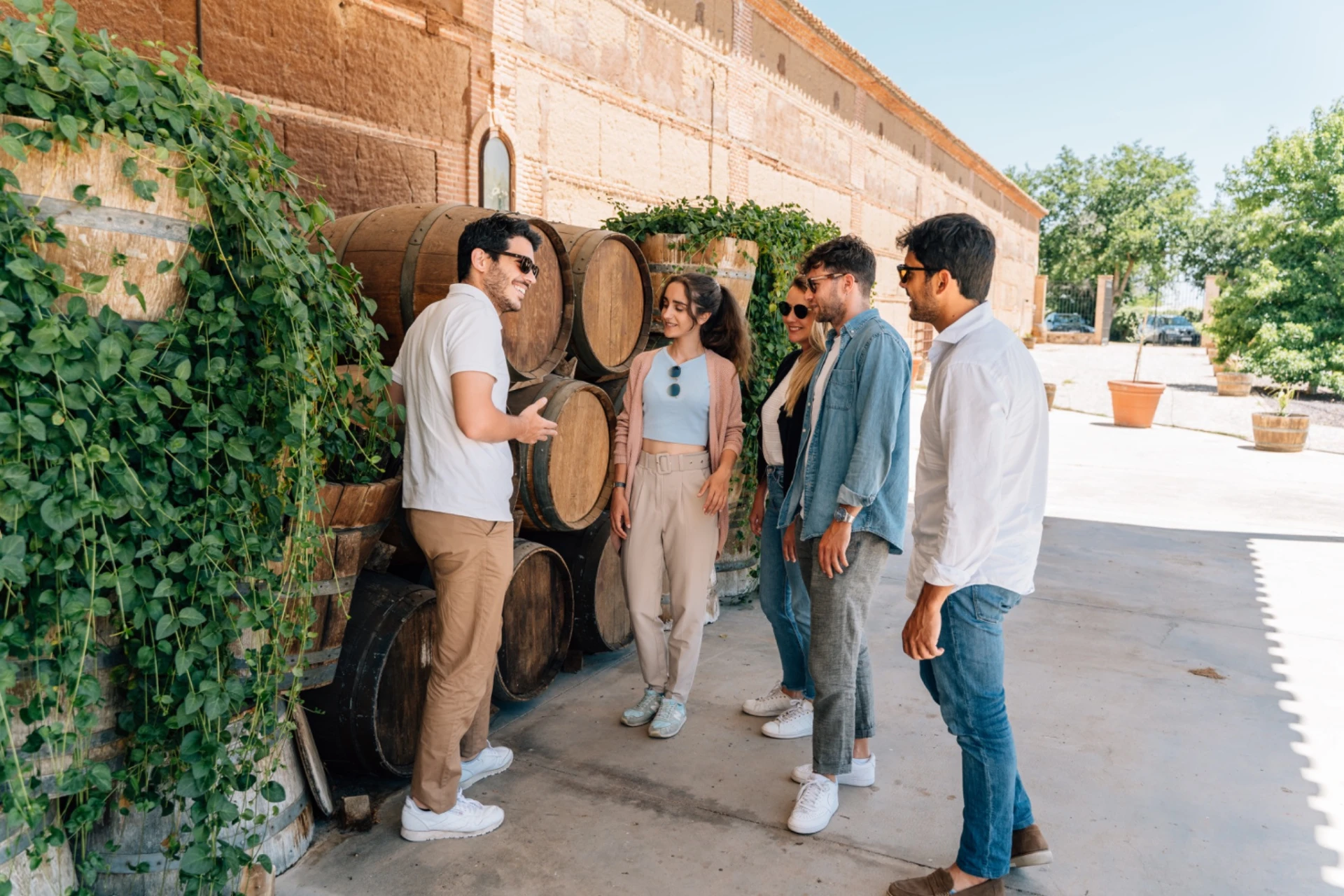 Small group of travelers with a local guide beside traditional oak wine barrels at a countryside winery near Toledo.